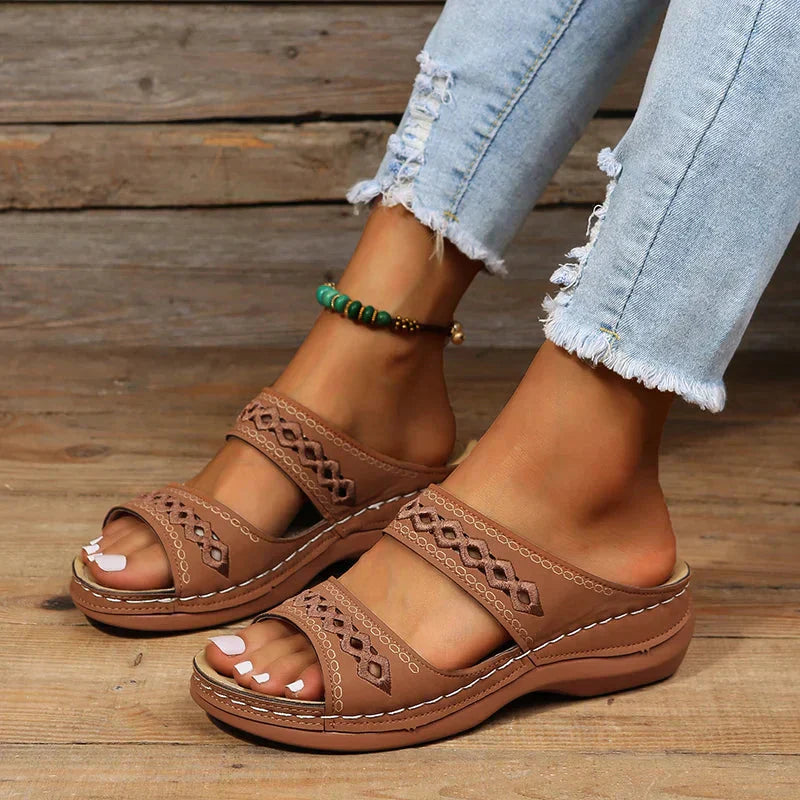 Women's Ezra open-toe slip-on wedge sandals in brown with cutout strap detailing, worn with jeans.