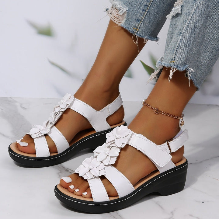 Loveleen white floral wedge sandals with an open toe, adjustable strap, and black sole, perfect for warm-weather outfits.