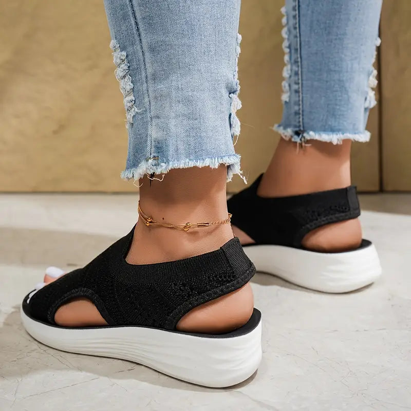 Women's black knit slip-on Soleil sandals with an open toe, side cutouts, and a cushioned white sole.