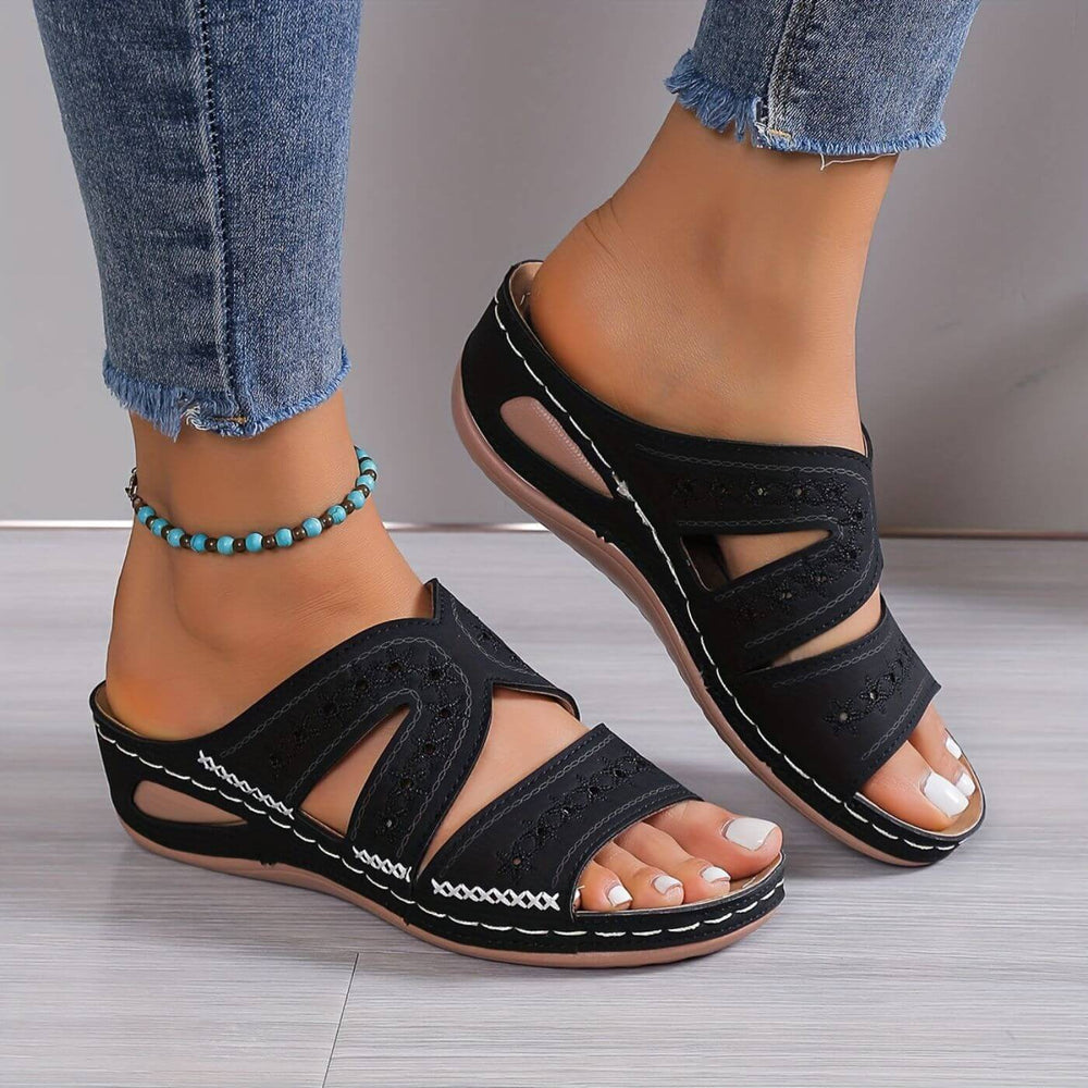 Soleva black embroidered wedge slide sandals with side cutouts and white stitching, worn with jeans.