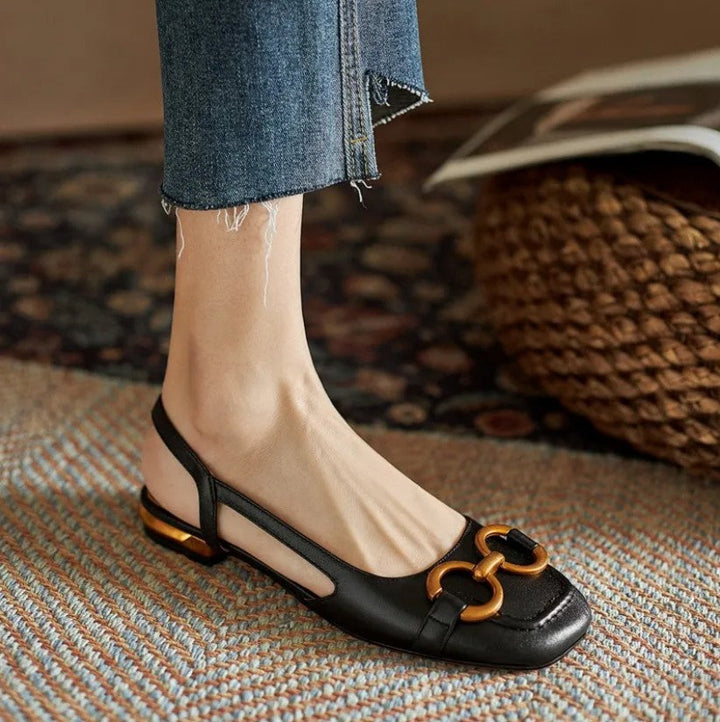 Verena black leather slingback buckle flats with a closed toe, low flat heel, and gold-tone buckle detail.