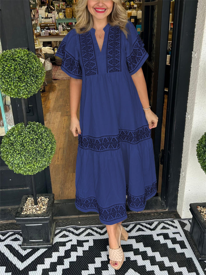 Woman in a blue Abigail boho V-neck midi dress with black embroidered details, styled with nude sandals.