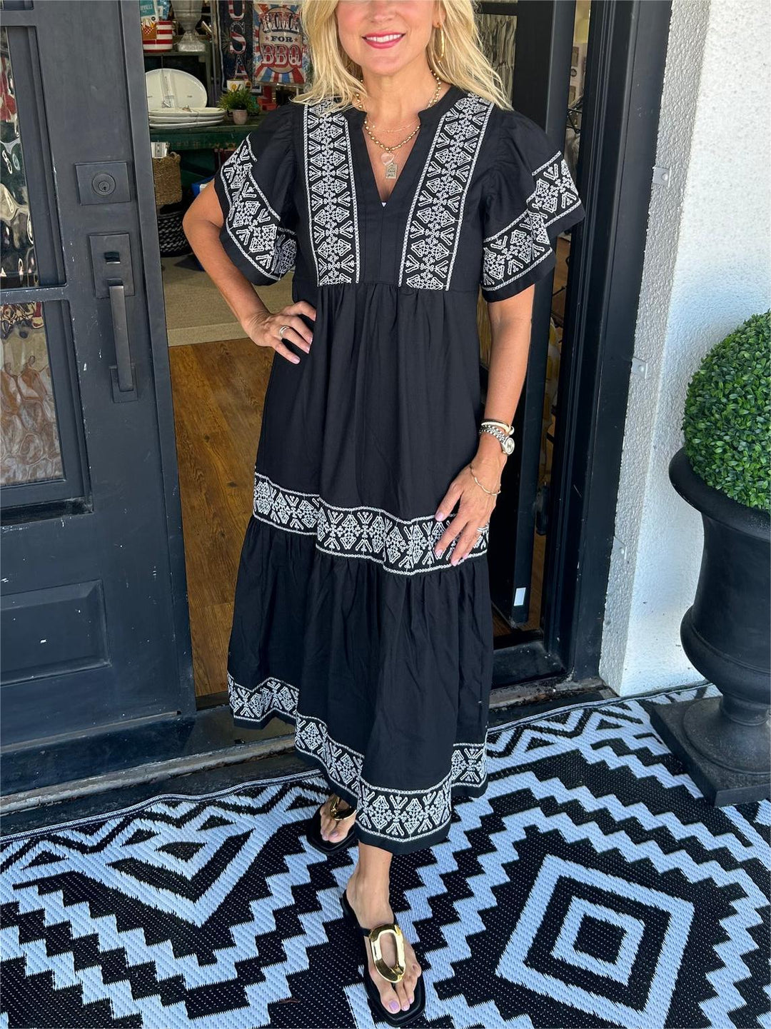 Woman in a black Abigail boho V-neck midi dress with white embroidered details, short sleeves, and tiered skirt.