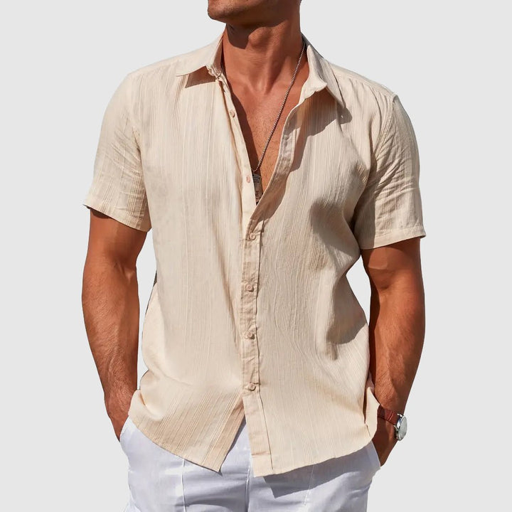 Men's Asher short sleeve linen button-up shirt in beige with subtle textured stripes, worn with white pants.
