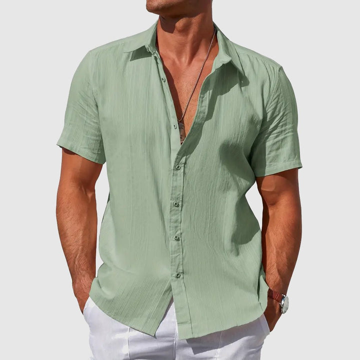 Men's Asher short sleeve sage green linen button-up shirt with subtle textured stripes, worn with white pants.