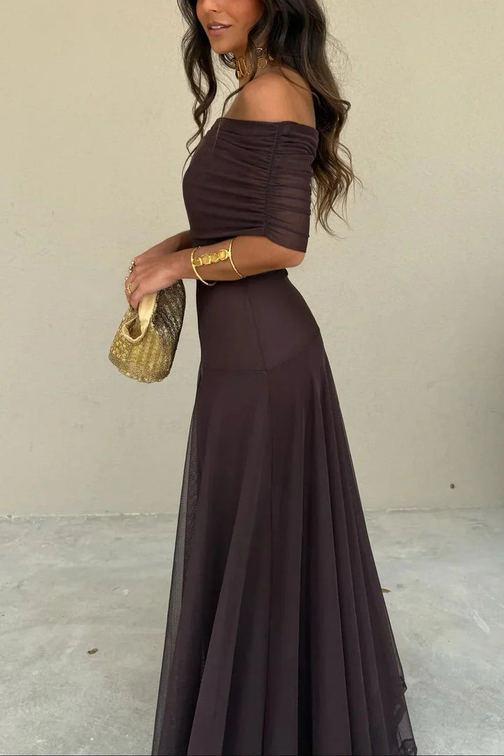 Aviana women's one-shoulder maxi dress in dark brown with draped bodice, flowing skirt, and gold accessories.