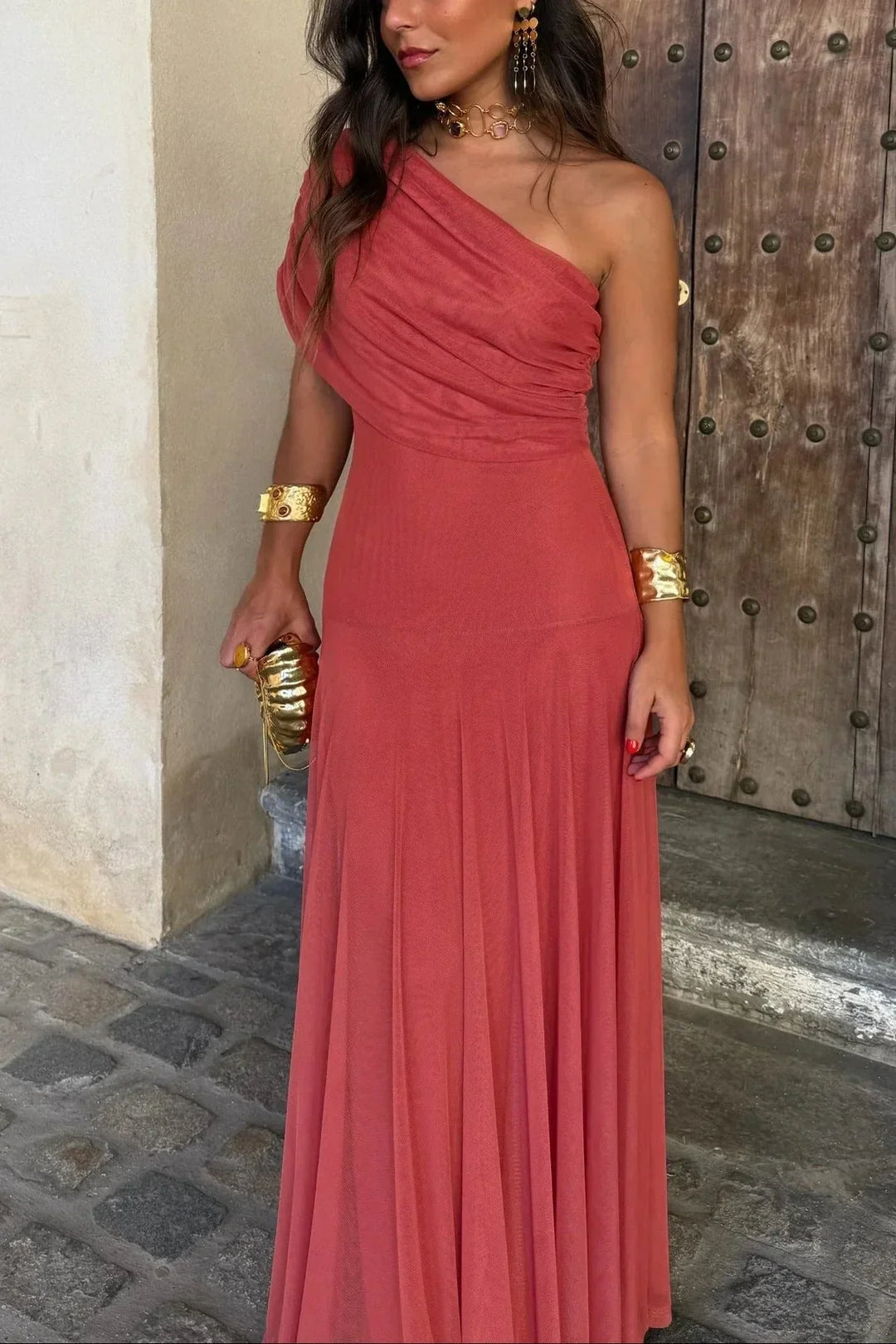 Aviana women's one-shoulder maxi dress in terracotta with draped bodice, paired with gold jewelry and clutch.
