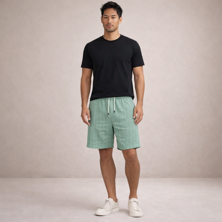 Man in black tee and light green textured linen drawstring shorts with white tie, above-knee length.