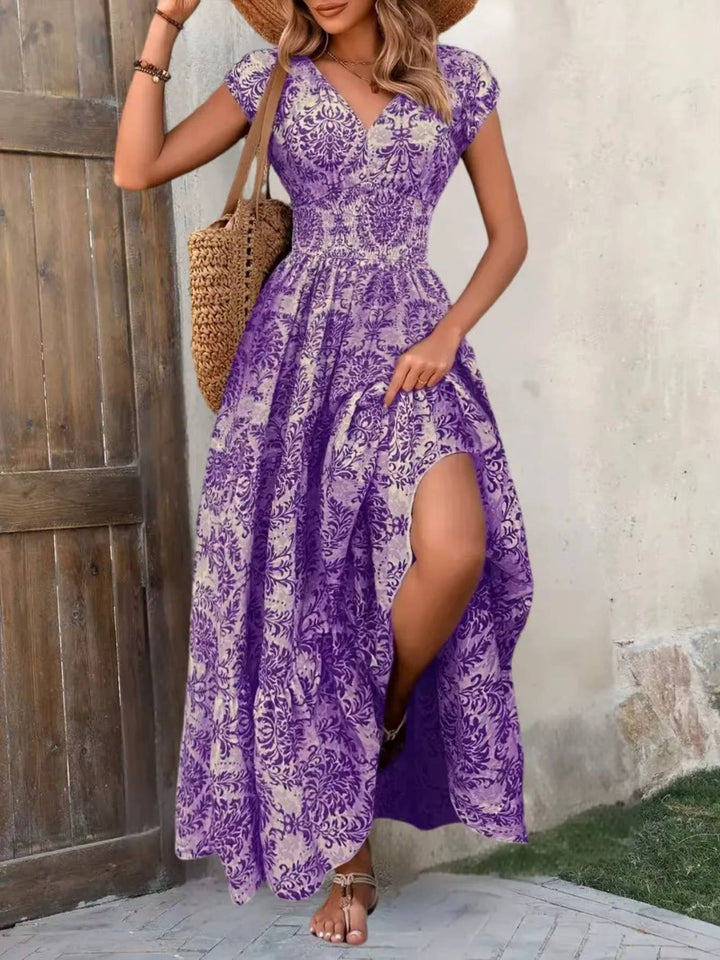 Women's purple V-neck maxi boho dress with ornate print, flutter sleeves, and side slit.