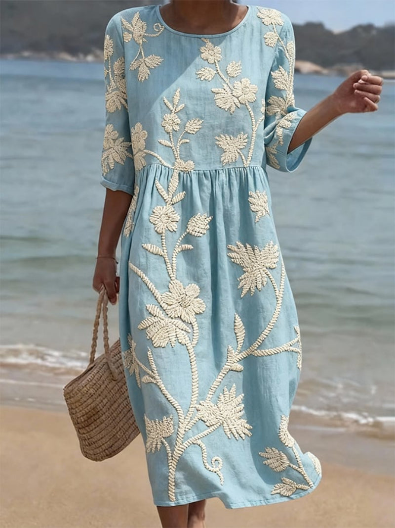 Women's light blue midi dress with white embroidered vintage floral design, three-quarter sleeves, and round neckline.