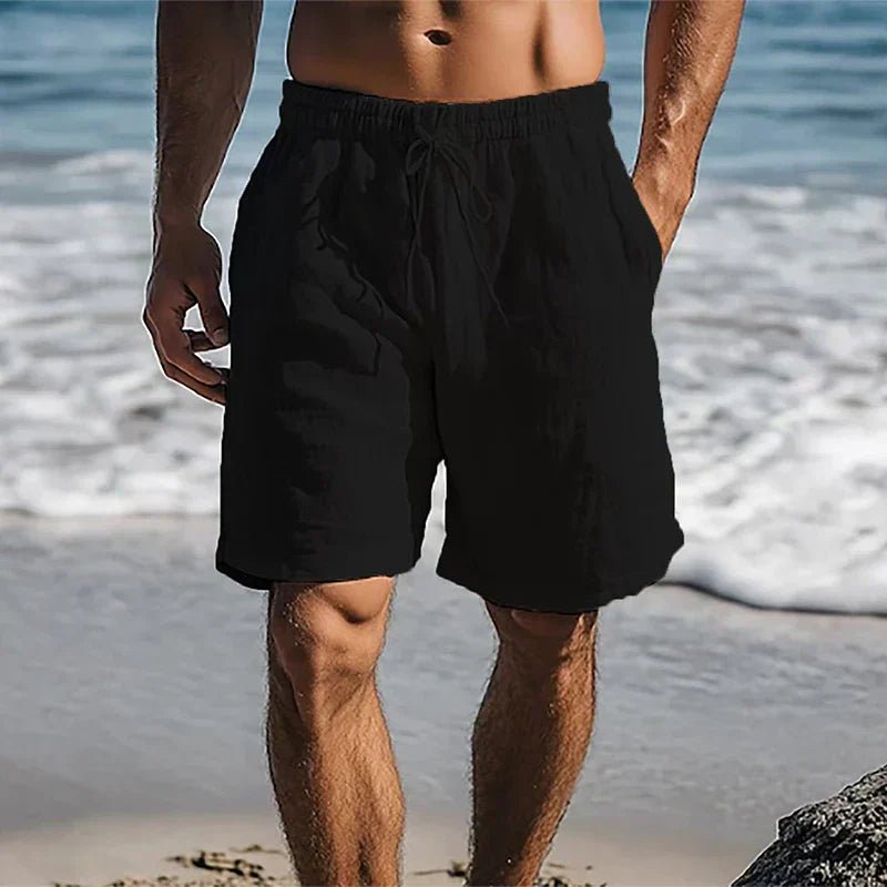 Men's black linen drawstring shorts with side pockets, worn on a beach.