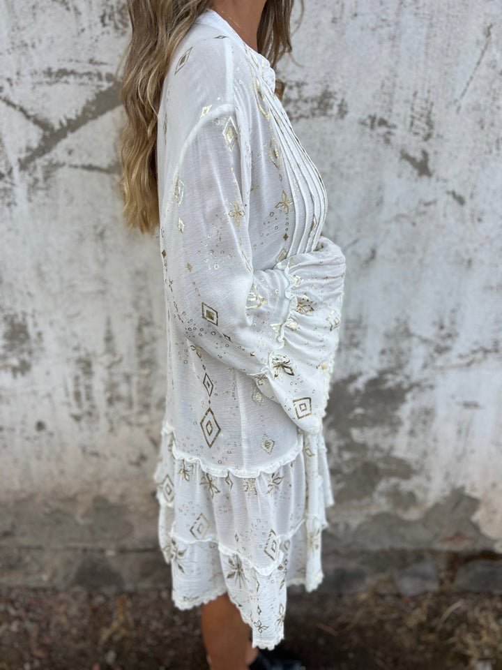 Women's white tiered boho V-neck dress with gold accents and three-quarter sleeves.
