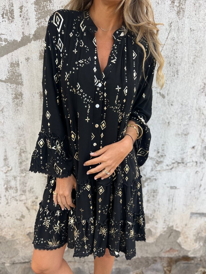 Black tiered boho V-neck dress with gold geometric print, three-quarter sleeves, and subtle gold-tone accents.