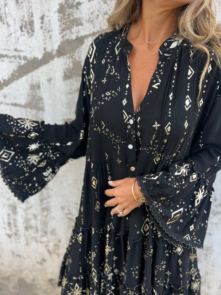 Women's black tiered boho V-neck dress with gold celestial print and three-quarter bell sleeves.