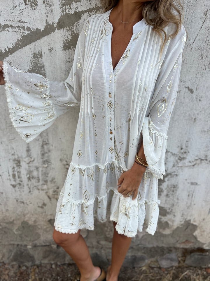 White tiered boho V-neck dress with gold accents, three-quarter sleeves, and ruffled hem.