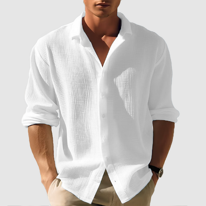 Men's white linen button-up shirt with a collared neckline and rolled long sleeves, paired with khaki pants.