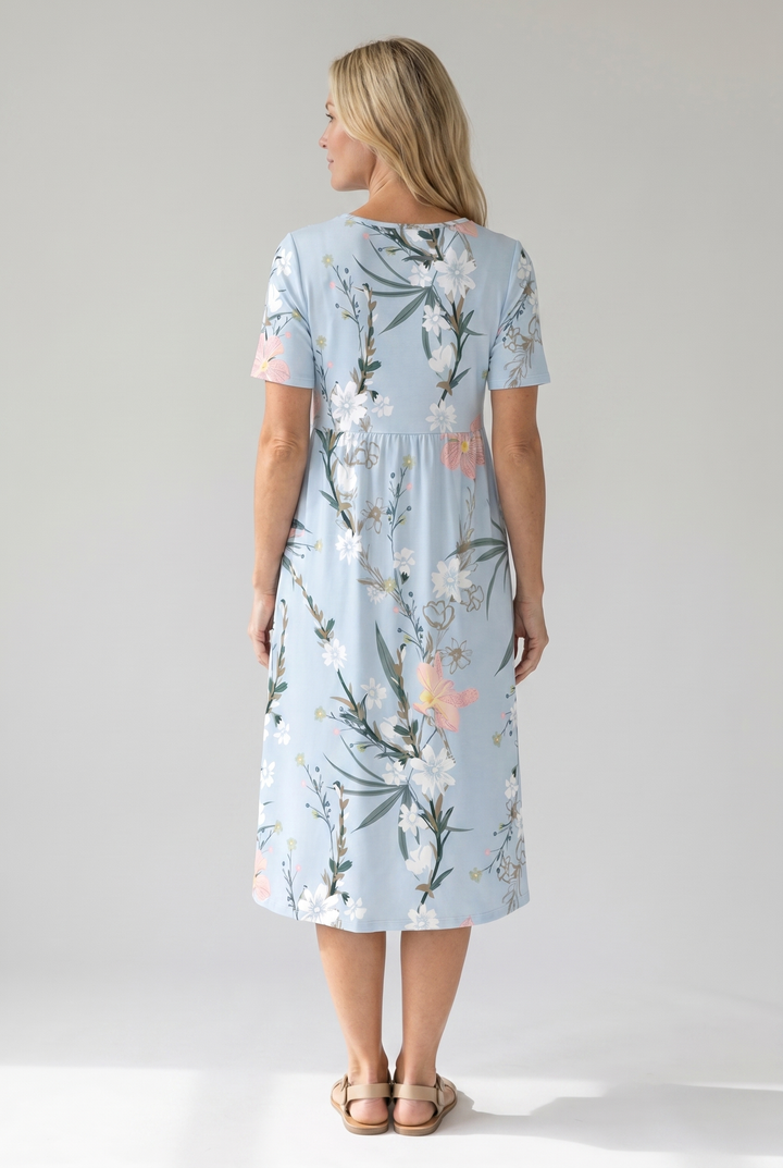 Woman in a light blue floral print midi dress with short sleeves and a gathered waist, viewed from the back.