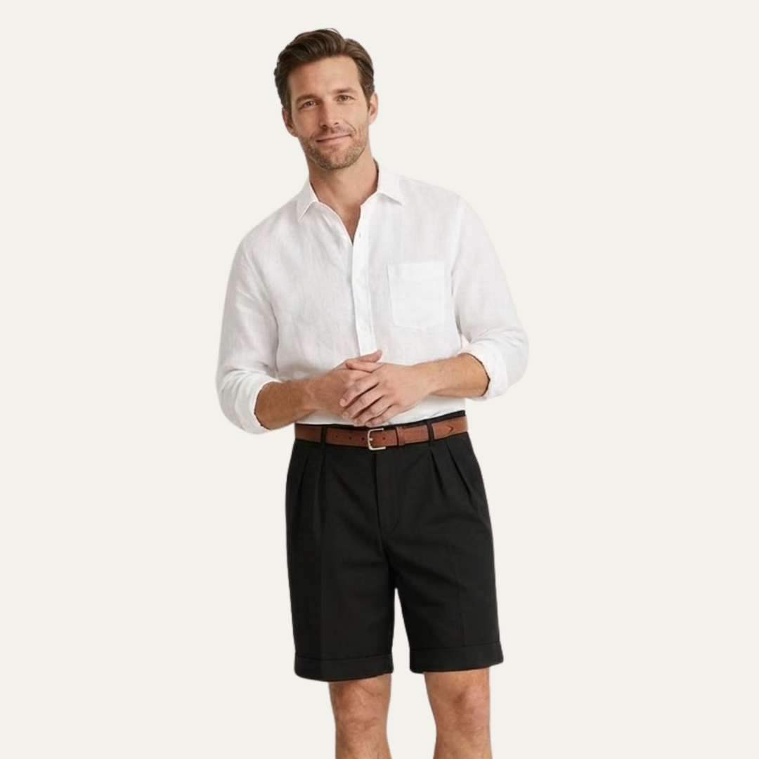 Men's Julian black pleated chino shorts with cuffed hems, worn with a brown belt and white linen shirt.