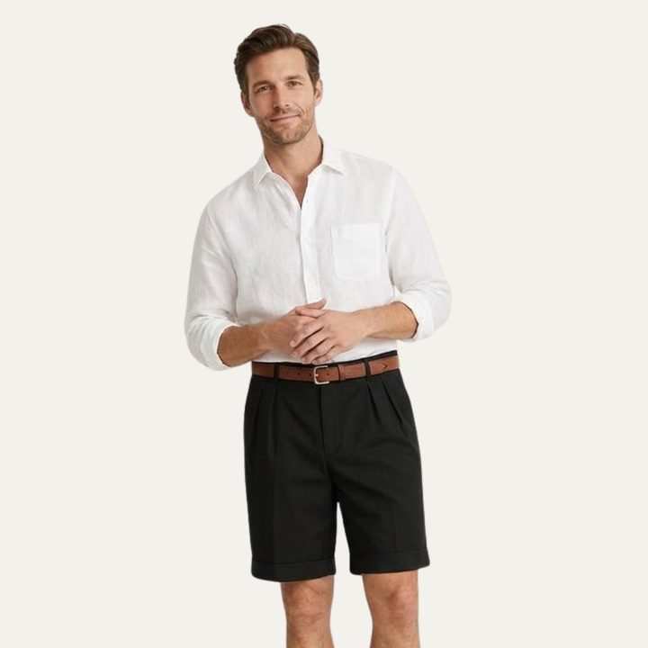 Men's Julian black pleated chino shorts with cuffed hems, worn with a brown belt and white linen shirt.