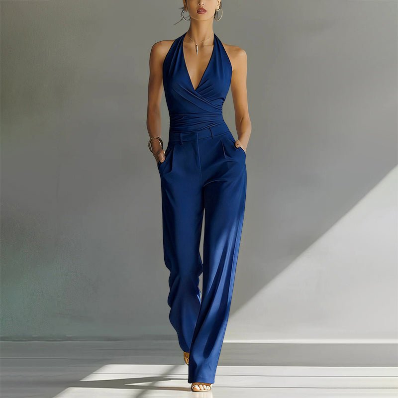 Woman wearing a navy blue halter wide-leg jumpsuit with a wrap-style bodice and side pockets.
