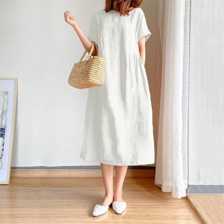 Woman in a white linen short sleeve midi dress, holding a straw bag.