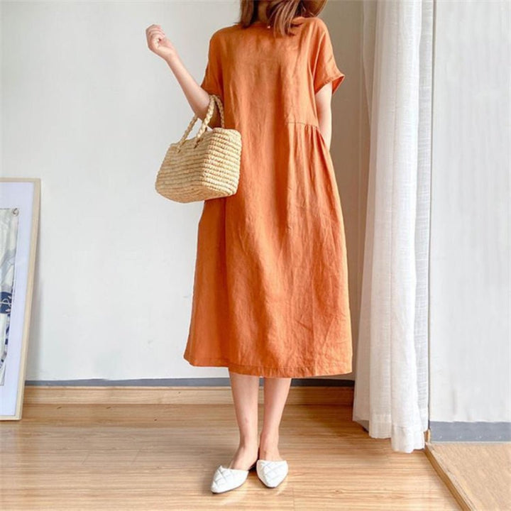 Women's Margot linen short sleeve midi dress in a warm orange hue, styled with a straw bag and white flats.