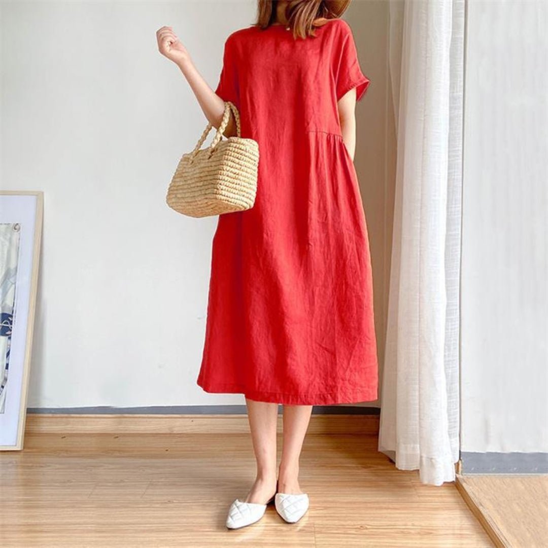 Woman in a red linen short sleeve midi dress, holding a straw bag, wearing white flats.