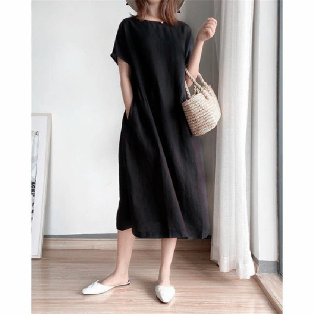 Woman wearing a black linen short sleeve midi dress with pockets, holding a woven bag.