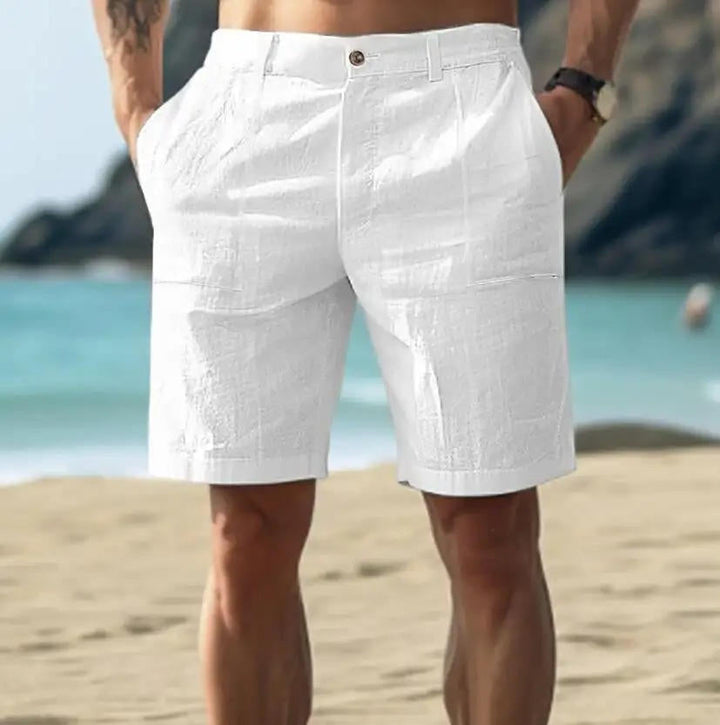 Men's white above-knee button-front shorts with front pockets, shown on a beach.
