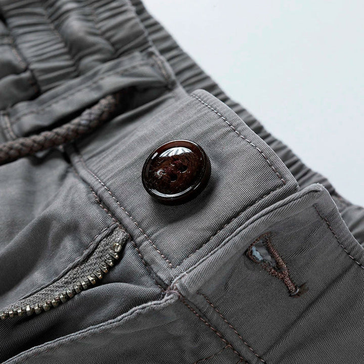 Close-up of men's gray drawstring cargo shorts with a dark brown button, zipper, and elastic waist.