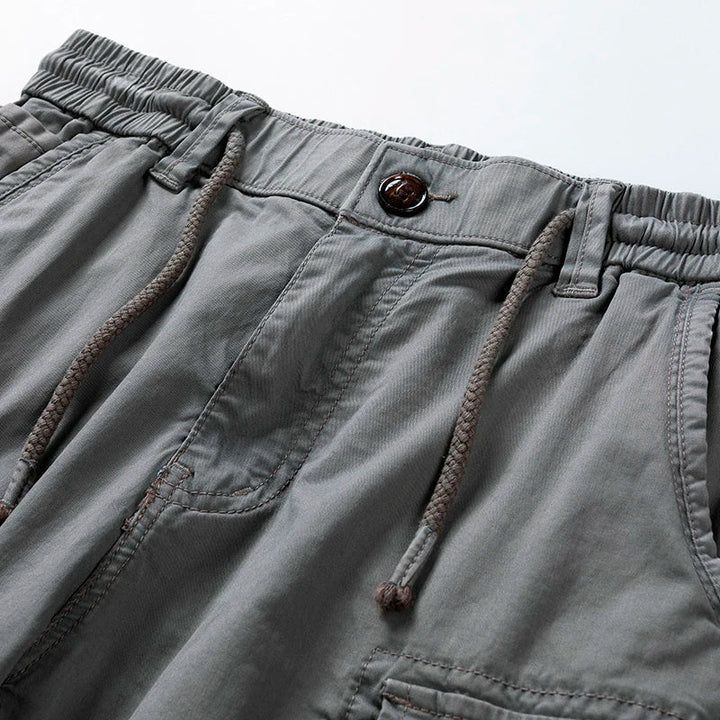Close-up of gray men's drawstring cargo shorts with an elastic waist, button, and visible stitching.