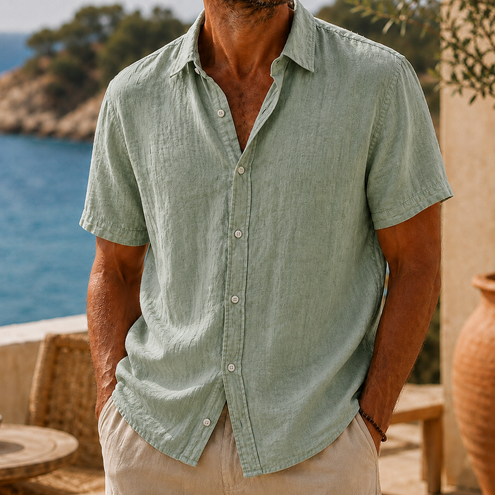 Men's Tyson sage green linen short sleeve button shirt with collared neckline, worn with beige pants.