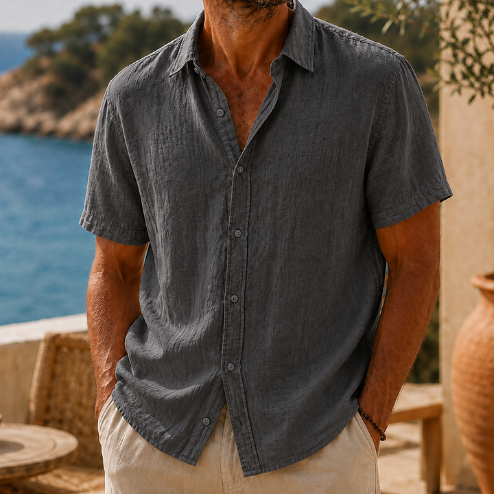 Men's charcoal gray linen short sleeve button-up shirt with a collared neckline, worn with light pants.