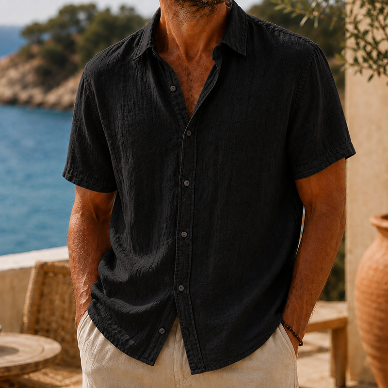 Men's black linen short sleeve button shirt with a collared neckline and textured fabric, paired with light pants.