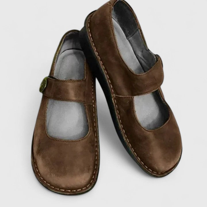 Brown leather orthopedic Mary Jane shoes with adjustable strap and decorative stitching.